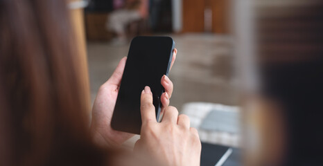 Young woman hands holding cell phone touching finger on mockup black blank display, empty screen for social media app ad at home. Mobile application tech concept, over shoulder view, closeup