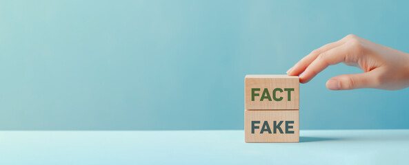 Fact or Fake concept, Hand choose fact wood cube on pastel blue background, April fools day