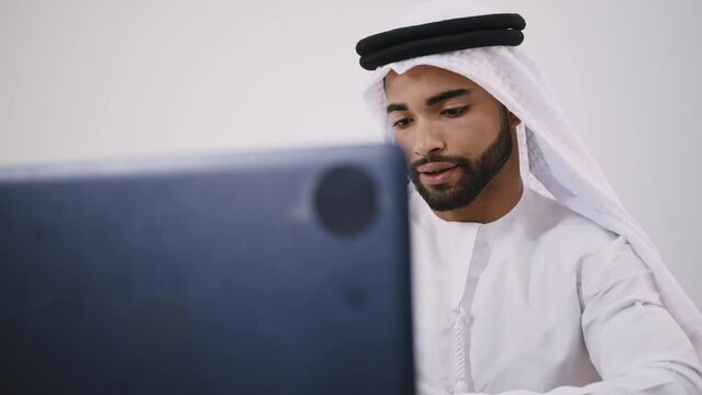 Handsome man with dish dasha working in his business office of Dubai. Portraits of a successful businessman in traditional emirates white dress. Concept about middle eastern cultures