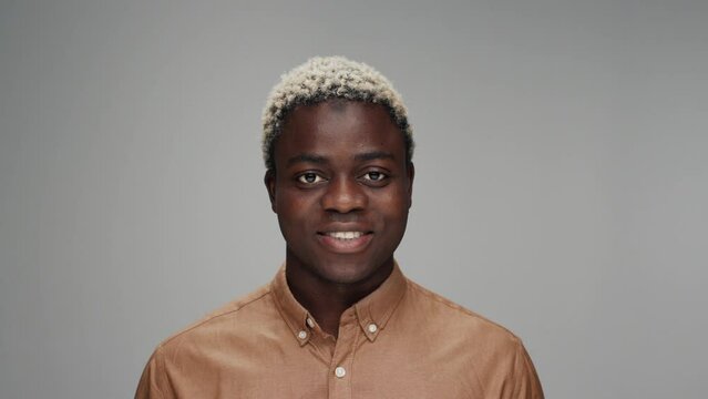 Portrait of Young Black Man Looking at Camera in Color Studio Shot. Adult Afro Boy Isolated Alone on Grey Background Close-up. African American Person Opening Beautiful Bright Eyes and Smiling Happy