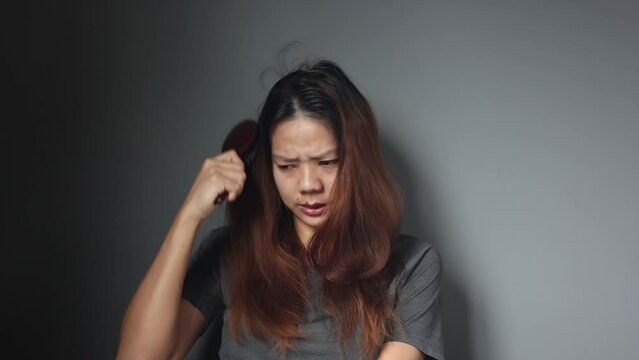 Asian girl with a comb and problem hair on gray background. Asian young woman holding brush, hairbrush with long loss hair problem after brushing.
