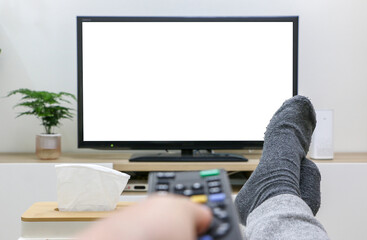 Feet up, first-person view of streaming and watching TV, movie night, pressing remote control, white blank TV screen in background. Clean and modern living room interior.