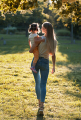 young mother with little daughter. Mom walks in the park with her daughter and holds her in her arms. view from the back - 645592437