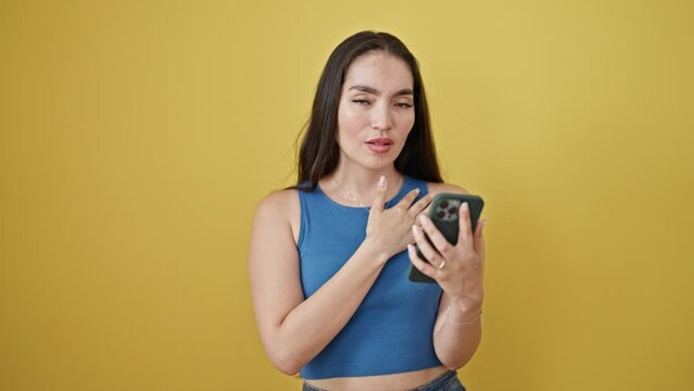 Young beautiful hispanic woman using smartphone saying no with head surprised over isolated yellow background