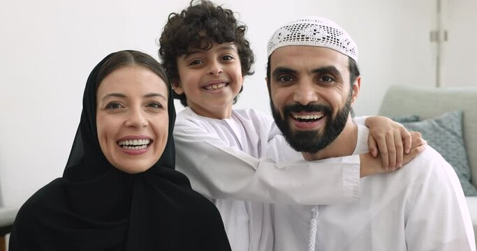 Middle-aged Muslim Couple With Preschooler 5s Pretty Son Posing For Camera At Home. Smiling Woman Wear Black Hijab Her Husband And Son In White Traditional Wear Looking At Cam. Happy Family Portrait