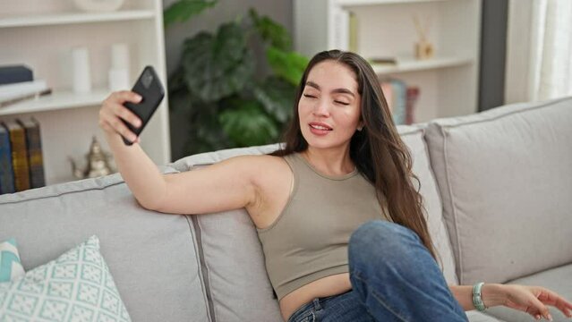 Young beautiful hispanic woman taking selfie picture with smartphone sitting on the sofa at home