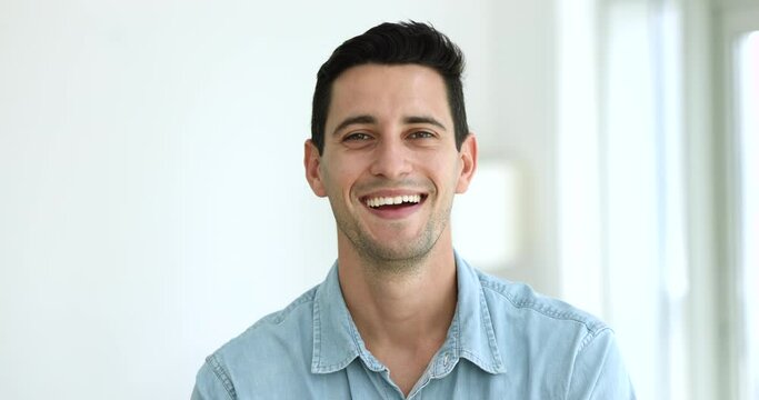 Head shot of happy authentic Hispanic man. Millennial male in casual shirt looks at camera standing indoors, having wide toothy smile advertise dental clinic services, portrait of handsome spanish guy
