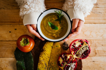Above view of woman hands holding cream vegetable soup on a wooden table with autumn decorations...