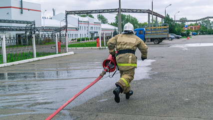 A firefighter with a fire barrel runs with a hose to supply water to extinguish the fire. Training of firefighters. A firefighter in protective clothing and a helmet with fire-fighting equipment.