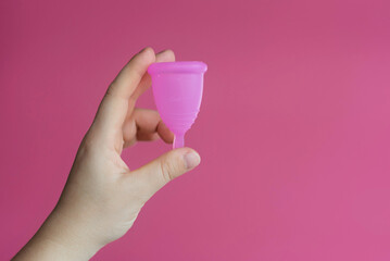 Reusable menstrual cup in a woman's hand on a delicate pink background. Сoncept female intimate...