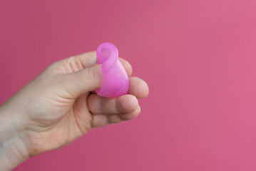 Reusable menstrual cup in the hands of a woman on a delicate pink background. How to fold the menstrual cup. Сoncept female intimate hygiene period products and zero waste. Minimalism. Copyspace.