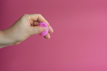 Reusable menstrual cup in the hands of a woman on a delicate pink background. How to fold the menstrual cup. Сoncept female intimate hygiene period products and zero waste. Minimalism. Copyspace.
