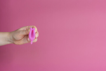 Reusable menstrual cup in the hands of a woman on a delicate pink background. How to fold the menstrual cup. Сoncept female intimate hygiene period products and zero waste. Minimalism. Copyspace.