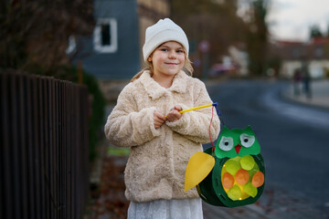 Little preschool kid girl holding selfmade traditional owl lanterns with candle for St. Martin...