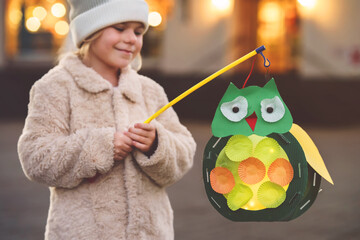 Little preschool kid girl holding selfmade traditional owl lanterns with candle for St. Martin...