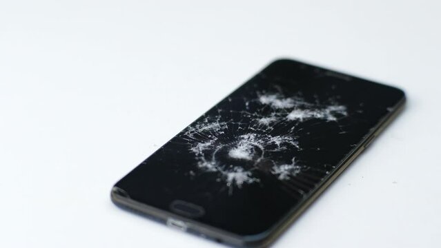 Broken black touch screen phone isolated on a white background. Broken glass with cracks from impact or smashed with a hammer. Smartphone damage, touch screen scratched with spider web.