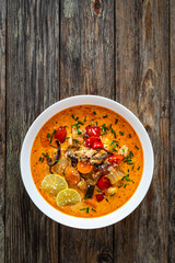 Tom Yum soup - Thai soup with chicken breast nuggets and noodles on wooden table
