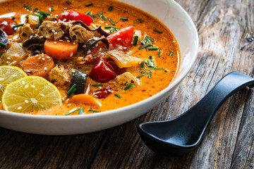 Tom Yum soup - Thai soup with chicken breast nuggets and noodles on wooden table
