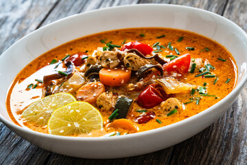 Tom Yum soup - Thai soup with chicken breast nuggets and noodles on wooden table
