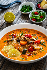 Tom Yum soup - Thai soup with chicken breast nuggets and noodles on wooden table
