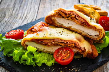Milanesa Napolitana - fried breaded cutlet with ham, mozzarella cheese and tomato sauce on wooden background
