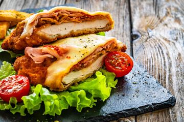 Milanesa Napolitana - fried breaded cutlet with ham, mozzarella cheese and tomato sauce on wooden background
