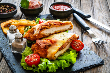 Milanesa Napolitana - fried breaded cutlet with ham, mozzarella cheese and tomato sauce on wooden background

