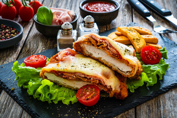 Milanesa Napolitana - fried breaded cutlet with ham, mozzarella cheese and tomato sauce on wooden background
