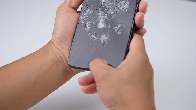 Female hand holding a smartphone with a broken screen and touching the screen isolated on white background. Smartphone damage, touch screen scratched with spider web.