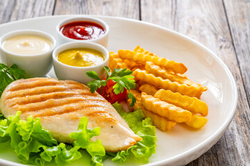 Grilled chicken breast, French fries and fresh vegetables on wooden table
