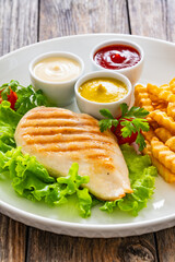 Grilled chicken breast, French fries and fresh vegetables on wooden table
