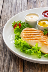 Grilled chicken breast, French fries and fresh vegetables on wooden table
