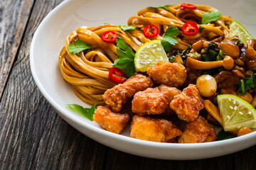 Asian food - chicken nuggets, noodles and fried shimeji mushrooms on wooden table
