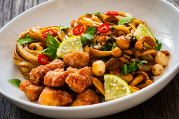 Asian food - chicken nuggets, noodles and fried shimeji mushrooms on wooden table
