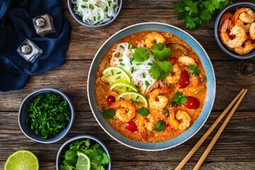 Tom Yum soup - Thai soup with prawns and rice noodles on wooden table

