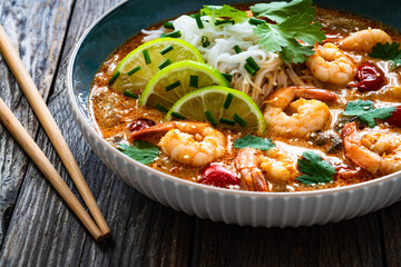 Tom Yum soup - Thai soup with prawns and rice noodles on wooden table

