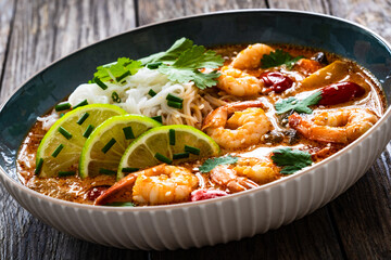 Tom Yum soup - Thai soup with prawns and rice noodles on wooden table

