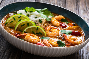 Tom Yum soup - Thai soup with prawns and rice noodles on wooden table

