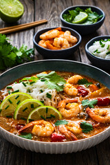 Tom Yum soup - Thai soup with prawns and rice noodles on wooden table

