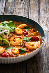 Tom Yum soup - Thai soup with prawns and rice noodles on wooden table


