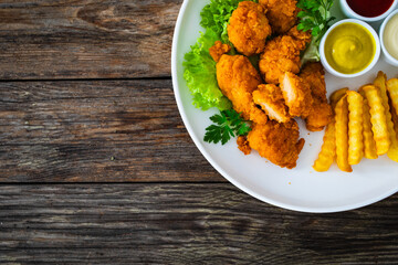 Seared breaded chicken nuggets with French fries on wooden table
