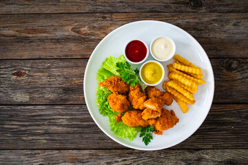 Seared breaded chicken nuggets with French fries on wooden table
