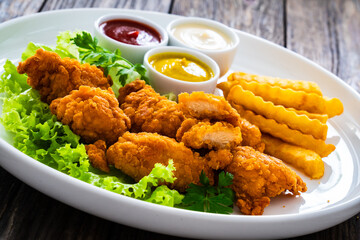Seared breaded chicken nuggets with French fries on wooden table
