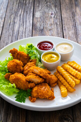 Seared breaded chicken nuggets with French fries on wooden table
