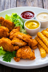 Seared breaded chicken nuggets with French fries on wooden table
