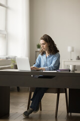 Serious young business employee woman typing on laptop, working in home office, sitting at workplace table, chatting, using online job application, Internet technology for communication