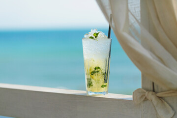 Glass of majito cocktail on terrace against blue sea. Cool drink on hot sunny day in cafe by the sea