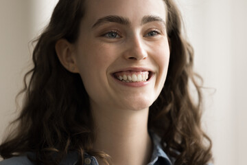 Happy pretty young adult Caucasian girl with wavy hair and bushy brows looking away with toothy smile, thinking, dreaming, laughing. Beautiful 20s female model cropped facial portrait