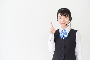 ヘッドセットをするベストにリボンタイの制服を着た、受付業務、事務業務の女性