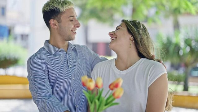 Beautiful couple surprise with bouquet of flowers kissing at park
